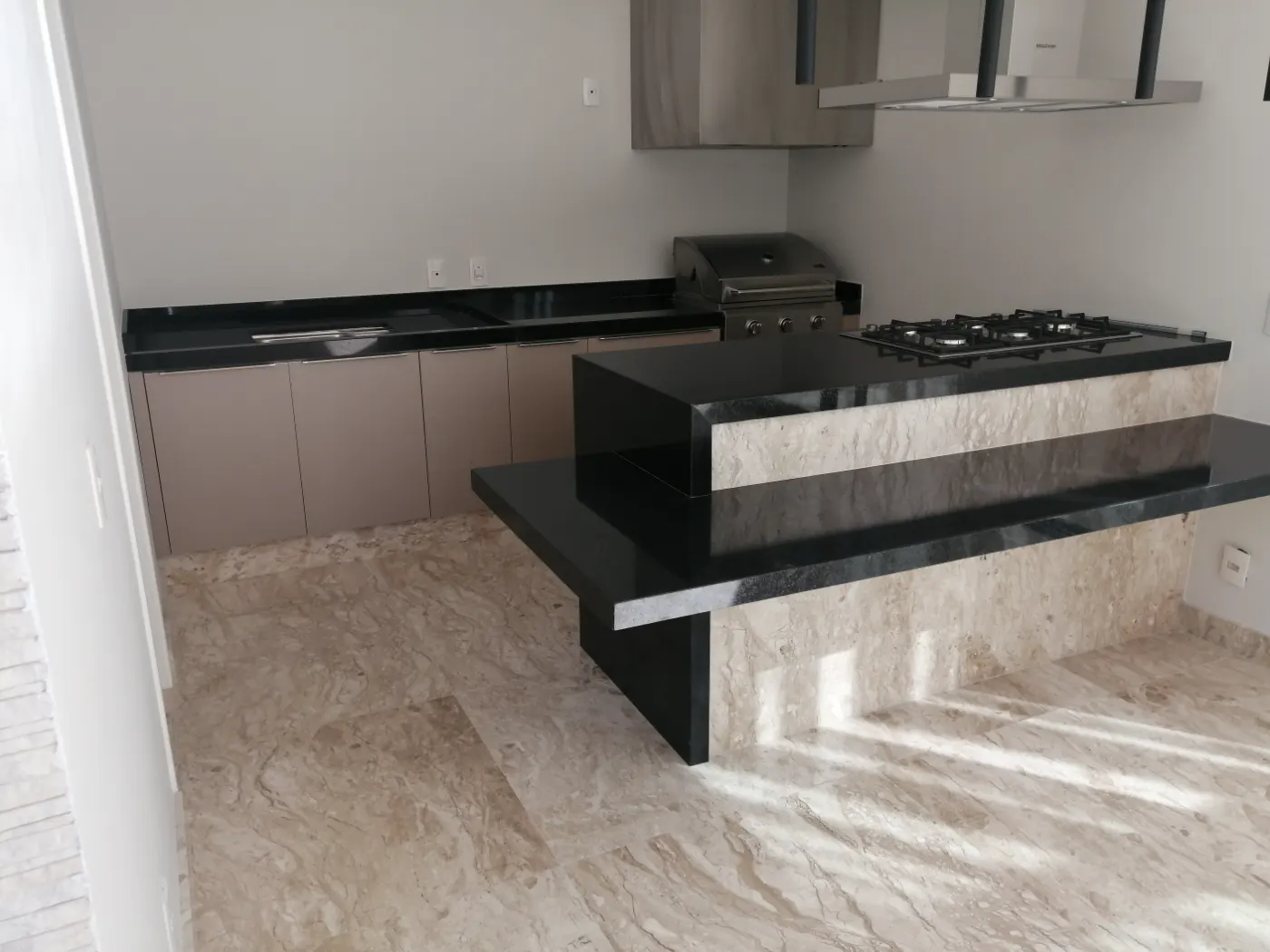Cozinha gourmet com bancada e ilha escuras e piso de pedra clara