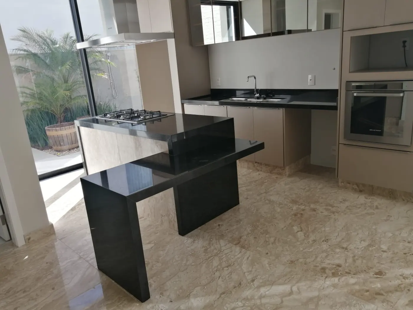 Ilha escura em cozinha com forno embutido e janelas para o jardim