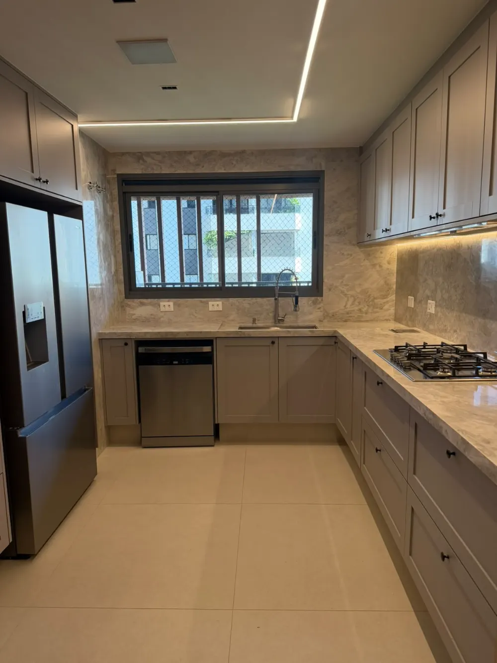 Cozinha em L com bancada e frontão de pedra, geladeira inox e luz embutida